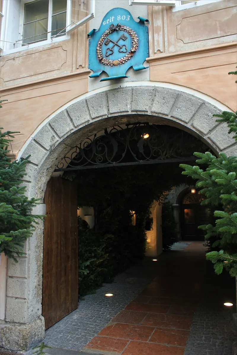 A stone archway into the Stiftskeller courtyard, with a blue sign showing two crossed keys and the words seit 803.