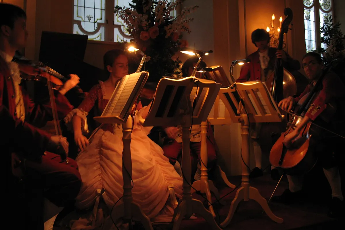 Musicians in red and cream period costume play violins, a double bass and a cello by candle-style lamps in the Stiftskeller; a photograph of a concert from 2007.