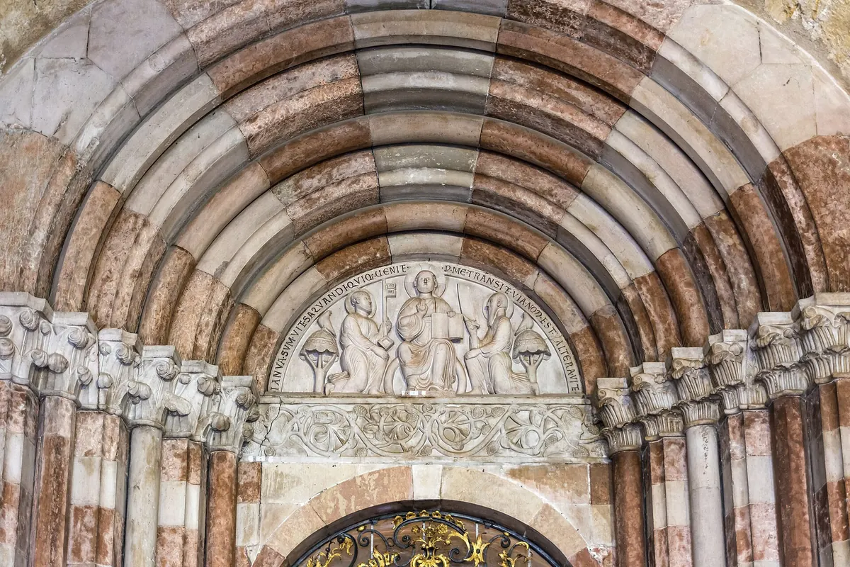 The stone portal of St. Peter's abbey church, with banded round arches and a carved relief of three seated figures.